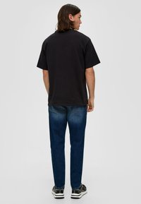 Schwarzes Baumwoll-T-Shirt mit kurzen Ärmeln und Rundhalsausschnitt, kombiniert mit dunkelblauen Jeans und schwarzen Sneakers mit weißen Akzenten.