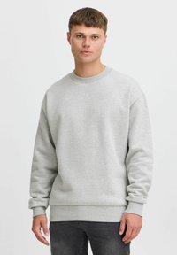 Sweat-shirt en coton gris à manches longues, avec un col et des poignets côtelés, et une coupe décontractée. Porté avec un jean gris foncé. Design simple sans motifs.