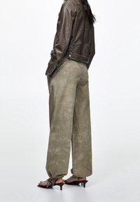 Bruine leren jas met een kort model, gecombineerd met losse, getextureerde olijfgroene broek en zwarte sandalen met hak.