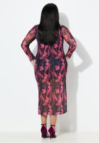 Vestido floral transparente con mangas largas, que presenta un fondo oscuro y un patrón de flores en un vibrante color rosa. Combinado con sandalias de tacón alto moradas.
