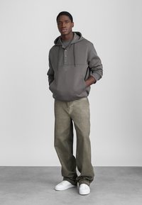 Hanorac gri cu buzunar frontal și placket cu trei nasturi, asortat cu pantaloni largi de culoare verde măsliniu și adidași albi. Design simplu și croială lejeră.