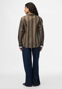 Camicia a maniche lunghe a righe marrone e bianca con controspallina, polsini abbottonati e vestibilità comoda, abbinata a pantaloni a gamba larga in denim scuro.