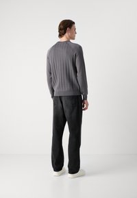 Hellgrauer Strickpullover mit gerippter Textur, Rundhalsausschnitt und langen Ärmeln, kombiniert mit schwarzer Jeanshose und weißen Turnschuhen.