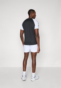 Svart-hvitt trenings T-skjorte med korte ermer, med rund hals og logo på siden. Kombinert med hvite shorts og joggesko.