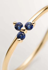 Brazalete de oro con tres piedras preciosas azules redondas dispuestas en un arreglo agrupado. Acabado suave con textura pulida, creando un aspecto moderno.