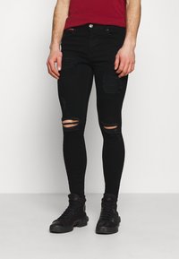 Jeans skinny negros con detalles desgastados, que incluyen múltiples desgarros. Fabricados en denim, presentan un diseño tradicional de cinco bolsillos y botón de metal.