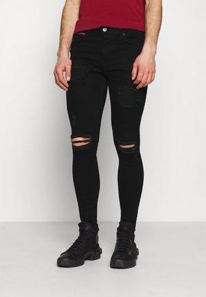 Jeans skinny negros con detalles desgastados, que incluyen múltiples desgarros. Fabricados en denim, presentan un diseño tradicional de cinco bolsillos y botón de metal.