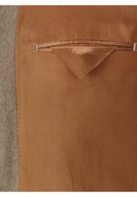 Brauner Stoff mit glatter Textur, einer kleinen dreieckigen Tasche und kontrastierendem grauem Filz auf einer Seite. Die genähten Kanten sind sichtbar.