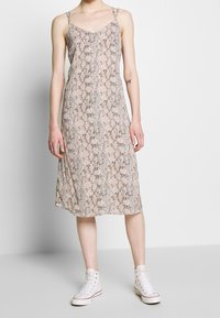 Midi-mekko käärmeennahkakuviolla pehmeästä ja kevyestä kankaasta. Ominaisuuksina ohuet hihnat ja rento ponnet. Päällä valkoiset korkeavartiset tennarit kontrastiksi.