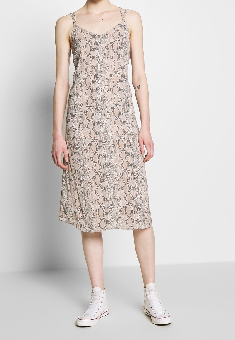 Midi-mekko käärmeennahkakuviolla pehmeästä ja kevyestä kankaasta. Ominaisuuksina ohuet hihnat ja rento ponnet. Päällä valkoiset korkeavartiset tennarit kontrastiksi.