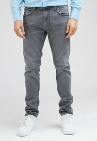 Grå denimjeans med slim fit, subtil blekning, fem fickor, förstärkta sömmar, bärs med vita sneakers.