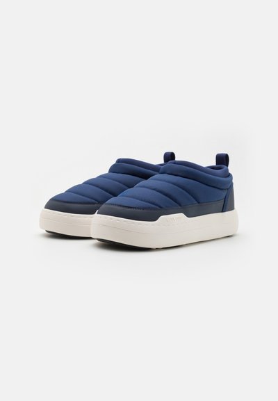 Tumši zilas slip-on sporta kurpes ar quilted auduma augšdaļu, mīkstu dizainu, baltu gumijas zoli un aizmugurējo cilpu vieglai uzvilkšanai.
