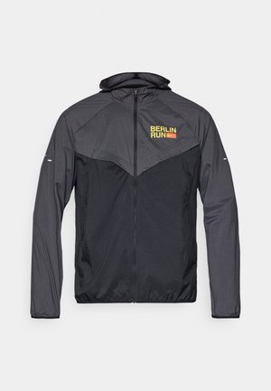 Moška tekaška jakna temno siva z kontrastno svetlo sivo ploščo. Ima kapuco, sprednji zadrgo in logo "BERLIN RUN" v rumeni barvi.