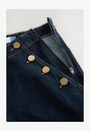 Pantalones vaqueros de mezclilla azul oscuro con cremallera, tres grandes botones de latón, costuras en contraste y una textura suave.