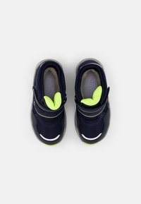 Marineblaue Sportschuhe mit einer strukturierten Oberseite, neon-grünen Akzenten an der Zunge und Klettverschlüssen. Hellgraue Laufsohle mit reflektierenden Details.