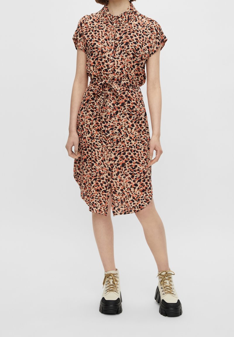 Femme portant une robe à manches courtes, boutonnée, avec un motif léopard et une taille nouée, associée à des bottines blanches à plateforme lacées.