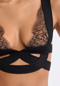 Sosten negro con ribete de encaje y un patrón floral, con aros acolchados y banda texturizada. Diseñado con un escote en V profundo y detalles con recortes.