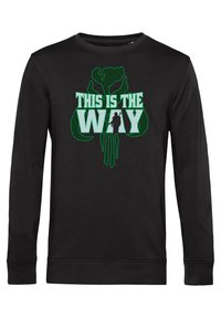 Sudadera negra de manga larga con un gran gráfico verde que presenta la frase "ESTE ES EL CAMINO" y una silueta, sobre un fondo texturizado.