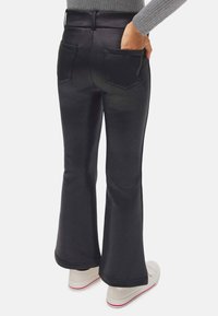 Pantalones acampanados negros con dos bolsillos traseros, una textura suave y una cintura ajustada. Combinados con zapatos casuales blancos con detalles en rojo.