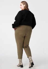 Zwart cropped sweatshirt met lange mouwen, gecombineerd met olijfgroene taps toelopende broek. Schoeisel met slangenprint en een chunkyhakken.