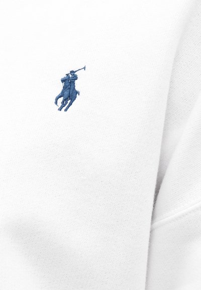 Tejido de sudadera blanca con un acabado texturizado, que presenta un pequeño logo bordado de un jugador de polo azul en el área del pecho izquierdo.