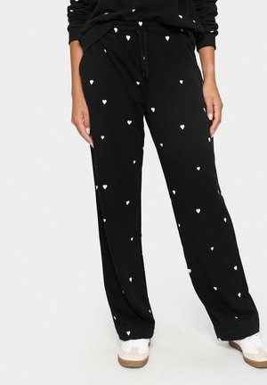 Pantaloni della tuta neri con piccoli motivi a cuore bianchi, vita elasticizzata e vestibilità rilassata, abbinati a sneakers bianche.