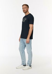 Marine T-shirt met witte grafische print, gecombineerd met lichtblauwe denim jeans en witte sneakers. Eenvoudig ontwerp, korte mouwen, casual pasvorm.