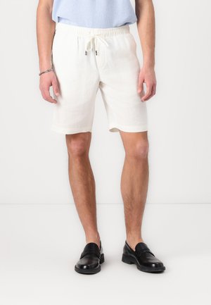 Calções brancos de linho com um cós elástico, cordão de ajuste e bolsos laterais, combinados com sapatos sociais de couro pretos.