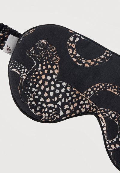 Μαύρη μάσκα ύπνου με υφασμάτινο λουράκι που διαθέτει σχέδιο λεοπάρ σε μπεζ και λευκές κηλίδες, περιμετρικά ραμμένη με μαύρη βελονιά.