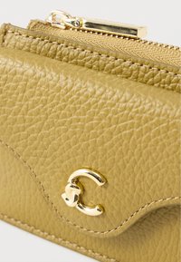 Portofel galben din piele texturată, cu închizătoare și fermoar aurii. Prezintă un design curbat și accente vizibile de cusături.