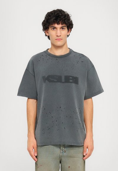 Overmaatse grijze T-shirt met versleten gaten, korte mouwen en een zwart "KSUBI" logo aan de voorkant. Zacht, textuurrijk katoenmateriaal.