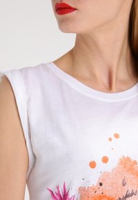 Biała bawełniana koszulka z okrągłym dekoltem i krótkimi rękawami, ozdobiona pomarańczowymi i różowymi wodnymi wzorami kwiatowymi.