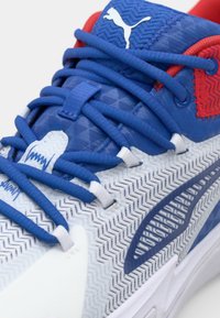 Blauwe sportsneaker met een gestructureerde bovenkant, witte accenten en een visgraatpatroon op de zool. Voorzien van rode details en opvallende veters.