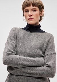 Szary dzianinowy sweter o luźnym kroju, z dekoltem w łódkę i opuszczonymi ramionami. Noszony na granatowym golfie. Miękka faktura, minimalne zdobienia.