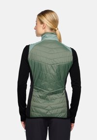 Gilet verde e nero con un design trapuntato, dotato di un colletto alto e pannelli laterali. Il tessuto appare morbido e leggero.