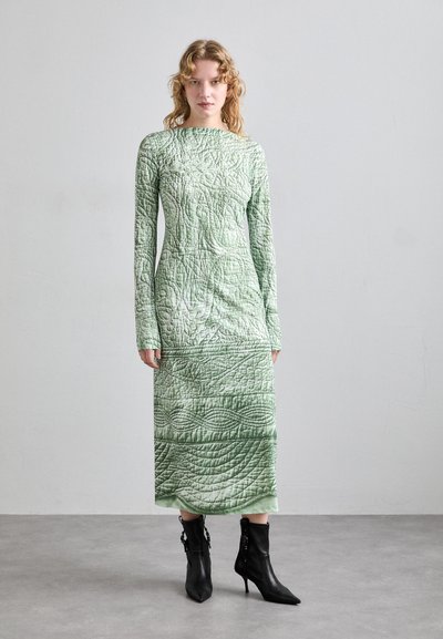 Quiltad, långärmad grön klänning med texturerade mönster; slutar vid smalbenet. Matchad med svarta spetsiga ankelstövlar.
