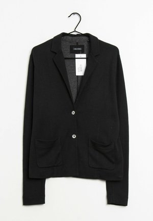 Schwarzer Strickblazer mit Reverskragen, zwei Knöpfen, Vordertaschen und sichtbarem Preisschild, das an einem schwarzen Kleiderbügel vor weißem Hintergrund hängt.