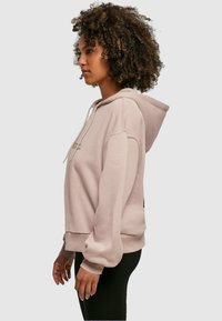 Pink hooded sweatshirt with long sleeves, ribbed cuffs, and kangaroo pocket. Soft texture with subtle branding on the chest.
