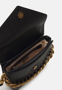 Černá kožená kabelka se zlatým řetízkovým popruhem. Má hladký povrch a béžový interiér s několika přihrádkami a zapínáním na cvok.