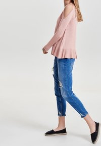 Hellrosa Cold-Shoulder-Pullover mit geripptem Saum, kombiniert mit ausgebeulten blauen Jeans. Das Model trägt schwarze Espadrilles mit Jute-Details.