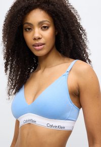 Ανοιχτό μπλε βαμβακερό μπραλέτο με V-λαιμόκοψη, λεπτές τιράντες και λευκή λωρίδα με το λογότυπο "Calvin Klein" κατά μήκος του κάτω μέρους.