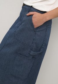 Falda de mezclilla a rayas azules con una cintura ajustada, bolsillo lateral y bolsillo trasero adicional. Textura suave y sutiles líneas verticales.