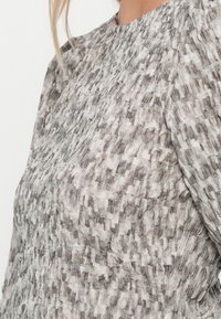 Γυναίκα που φοράει μπλούζα με μακριά μανίκια με υφή σε γκρι και λευκό καρό σχέδιο, κοντινό πλάνο που δείχνει τις λεπτομέρειες του υφάσματος και την εφαρμογή.