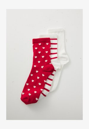 Drei gefaltete Socken gestapelt: rot mit weißen Herzen, weiß mit roten Streifen und schlicht weiß auf einem weißen Hintergrund.