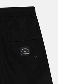 Mustad lühikesed püksid elastse vöökohtaga, tagumise taskuga. Taskusse on õmmeldud silt "KARL LAGERFELD PARIS". Sile tekstuur.