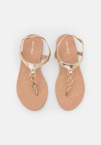 Kultaiset litteät sandaalit, joissa on teksturoitu beige sisäpohja. Ominaisuuksiin kuuluu linkitetty ketjuaksentti ja säädettävä nilkkaremmi. Suuri metallinen päällinen.