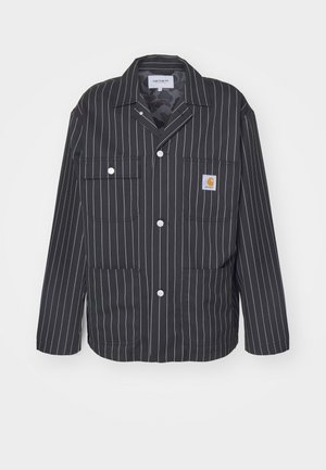 Schwarz-weiß gestreifte Jacke mit Kragen, ausgestattet mit zwei Brusttaschen, Druckknöpfen und einem Logo-Patch auf der linken Tasche.