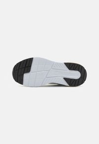 Suola di scarpa atletica in bianco e nero con un design in gomma testurizzata, caratterizzata da un modello di battistrada prominente e un logo. Aree lisce contrastano con le scanalature.