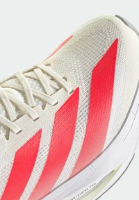Running shoe featuring a lightweight, textured off-white upper with prominent red stripes, laces, and a cushioned white sole.