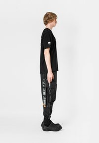 Camiseta negra de manga corta; pantalones cargo de corte holgado con múltiples bolsillos e impresiones gráficas; zuecos texturizados con patrones elevados.